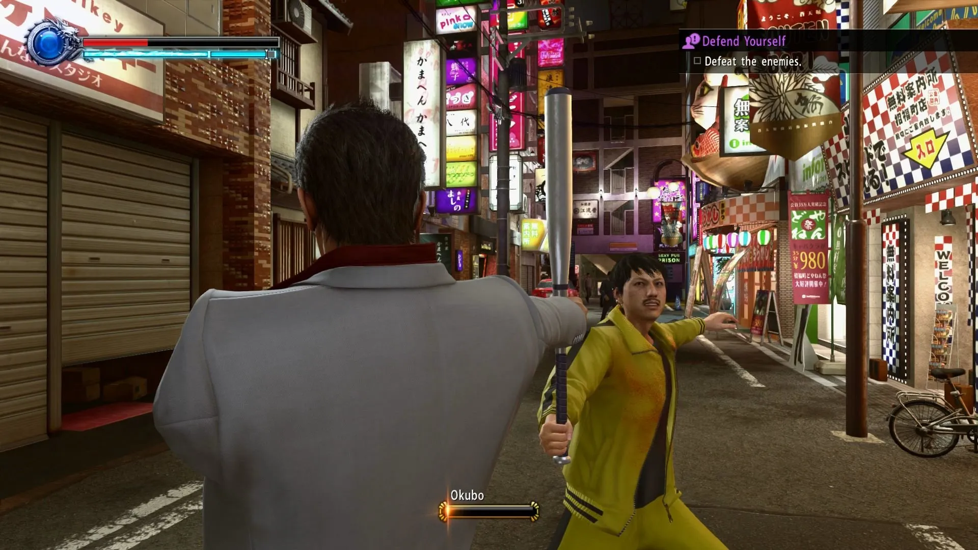 Captura Yakuza Kiwami – Kiryu Sostiene Un Bate Frente A Un Enemigo En Chandal Amarillo En Una Calle Japonesa
